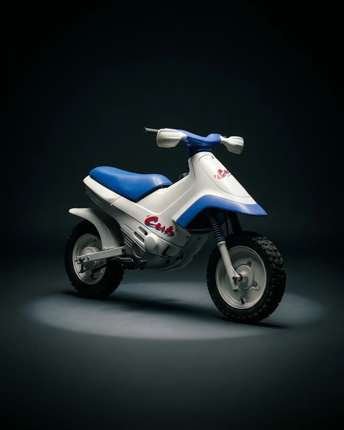 Studio rendering of a Honda Cub EZ90 from the collection: white bodywork, blue seat and accents, red Cub script, knobby tires, on a dark studio background.
